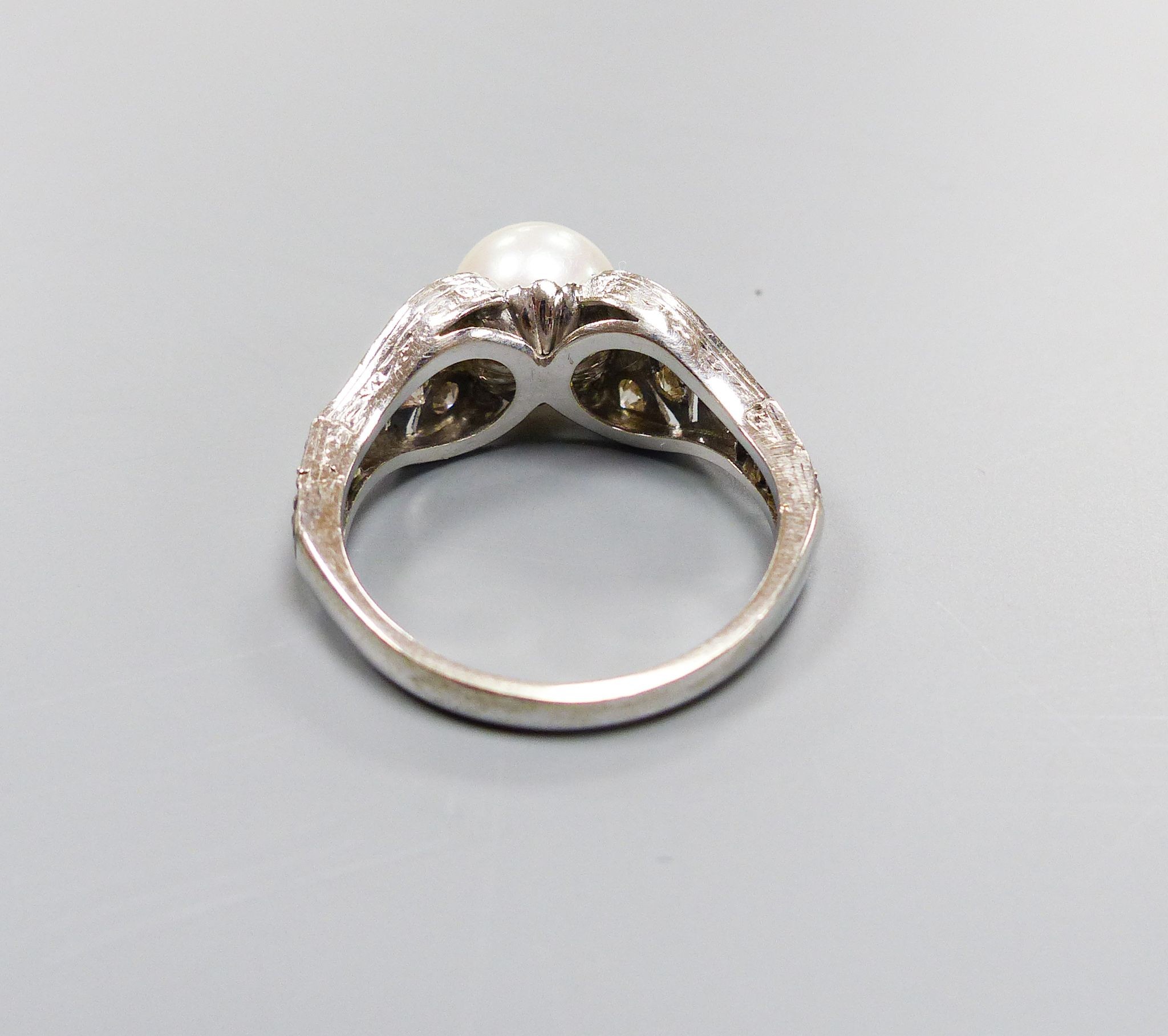 A modern 750 white metal and single stone cultured pearl dress ring, with diamond chip set pierced shoulders, size R/S, gross weight 5.5 grams.